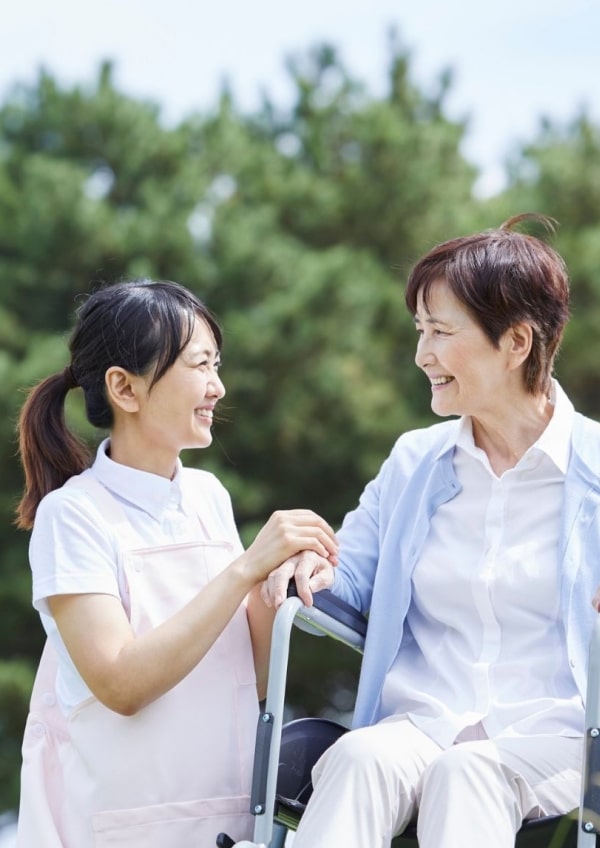 車椅子の高齢の女性のサポートをする女性介護士