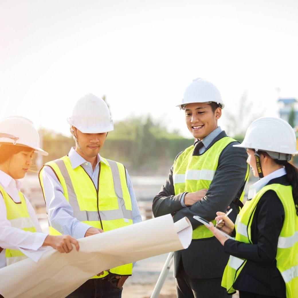 現場でヘルメットを被った男女の従業員が設計図を見て話をしている